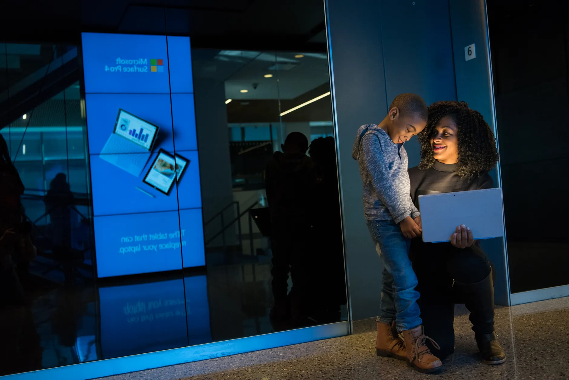 A smiling woman shows a boy something on a laptop in a tech-focused indoor environment.