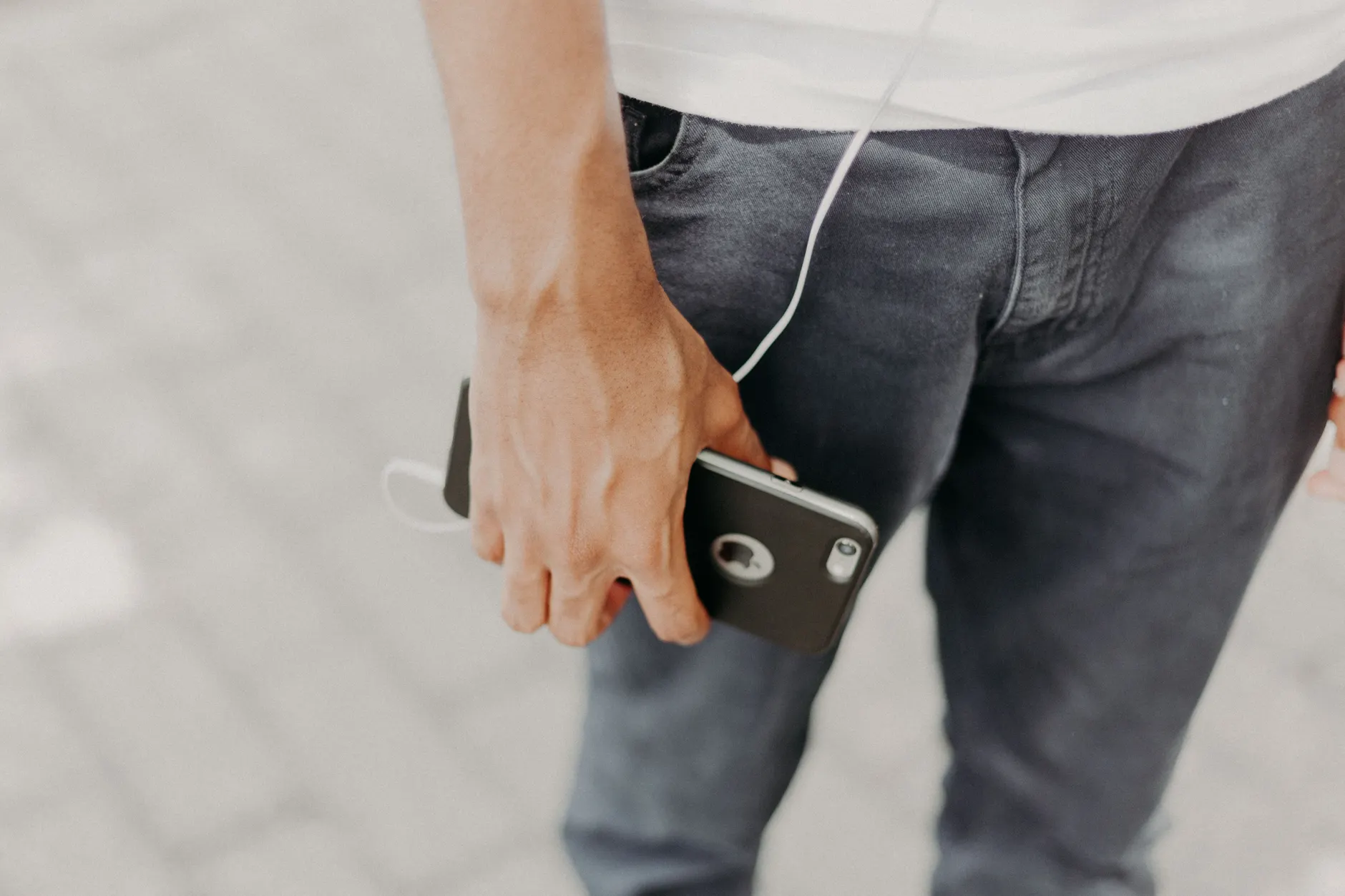 Close-up of a man holding a smartphone with headphones, showcasing modern tech and fashion.